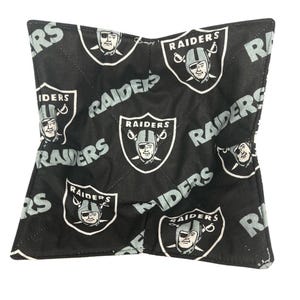 May include: Black and white Raiders bowl cozy. The cozy features a repeating pattern of the Raiders logo and the word "Raiders" in gray. The cozy is square-shaped with a quilted design.