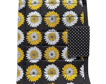 May include: Black quilted fabric with a daisy pattern in yellow and white. A small black square with white polka dots is attached to the side. The daisies are evenly spaced across the fabric.