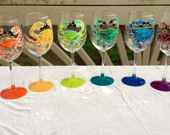 Puede incluir: Conjunto de ocho copas de vino con diseños de cangrejos pintados a mano. Cada copa presenta un cangrejo de color diferente con detalles intrincados. Las copas están dispuestas en un patrón de arcoíris, del rojo al morado.