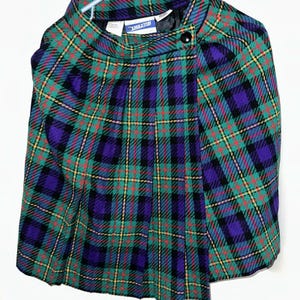 Pode incluir: Uma capa xadrez Pendleton em verde, roxo, vermelho e preto. A capa apresenta um fecho de botão e uma gola alta. O tecido tem um padrão xadrez clássico, e a peça de roupa está pendurada num cabide.