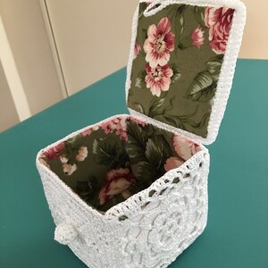 May include: A white crocheted box with a floral fabric lining. The box has a hinged lid with a white crocheted handle.
