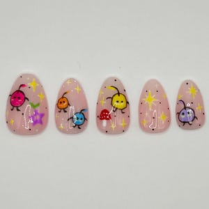 May include: Five pink oval-shaped false nails with different colorful cartoon bug designs. Each nail has a yellow star and black dots.