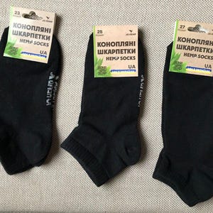 Może przedstawiać: Trzy pary czarnych skarpet konopnych z tekstem "КОНОПЛЯНІ ШКАРПЕТКИ HEMP SOCKS UA" na opakowaniu.