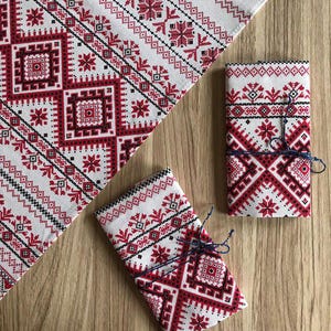 May include: Three white fabric napkins with red and black embroidered geometric patterns. The napkins are tied with blue string.