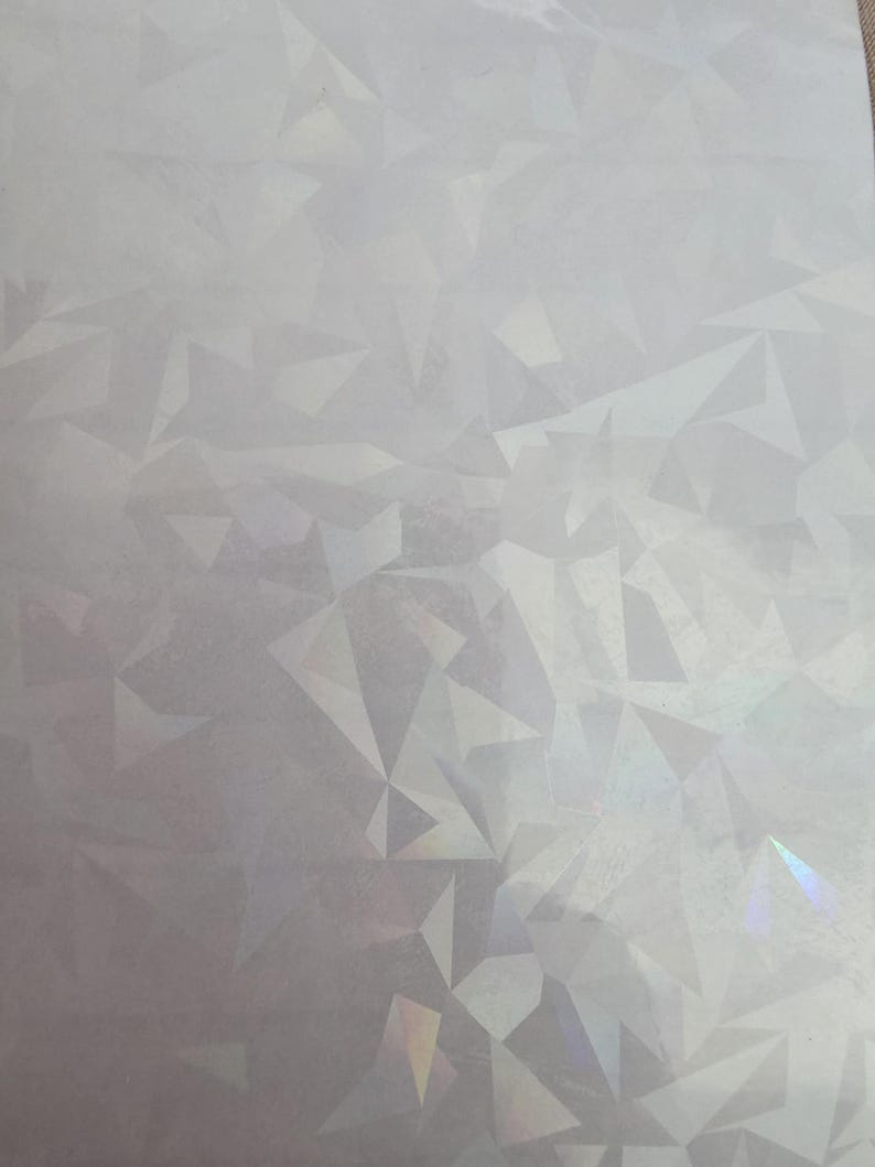 May include: A sheet of iridescent, geometric patterned paper. The design features a repeating pattern of irregular, multi-faceted shapes in shades of white and silver, with hints of rainbow iridescence.
