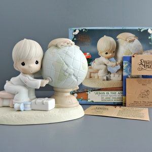 May include: A porcelain figurine of a child sitting on a stool, touching a globe. The base is textured, and a small white case sits nearby. The packaging box displays the text "JESUS IS THE ANSWER" and "ST. JUDE CHILDREN'S RESEARCH HOSPITAL."