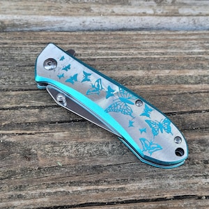 May include: A silver pocket knife with a blue butterfly design. The knife is closed and has a silver handle.