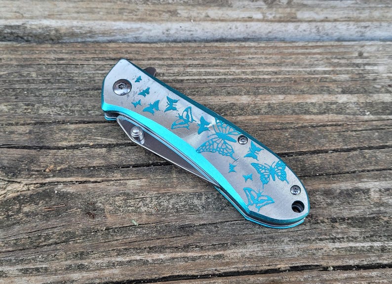 May include: A silver pocket knife with a blue butterfly design. The knife is closed and has a silver handle.