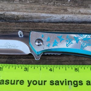 May include: A silver pocket knife with a turquoise handle. The handle is decorated with a pattern of butterflies. The knife is 7 inches long.