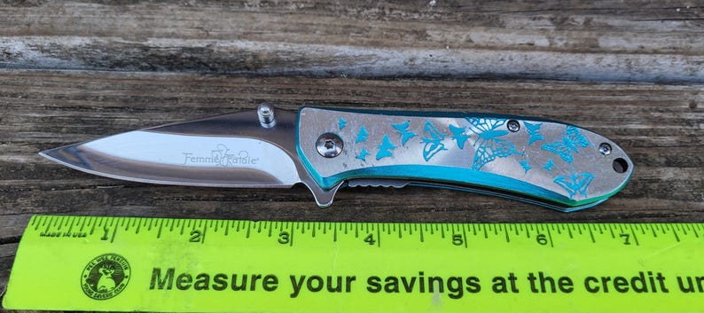 May include: A silver pocket knife with a turquoise handle. The handle is decorated with a pattern of butterflies. The knife is 7 inches long.