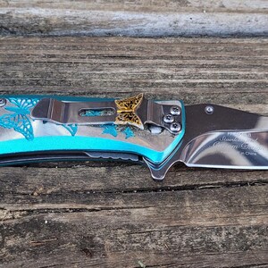 May include: A blue pocket knife with a butterfly design and a gold butterfly accent on the handle.