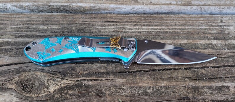 May include: A blue pocket knife with a butterfly design and a gold butterfly accent on the handle.