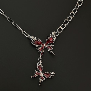 May include: A silver chain necklace with two red butterfly pendants. The butterflies are detailed and have a textured finish.