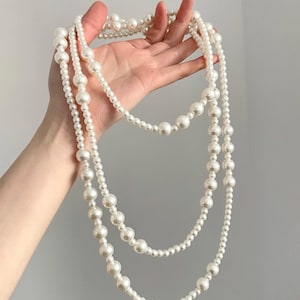 May include: A long white pearl necklace with three strands of pearls. The necklace is made of large and small pearls.