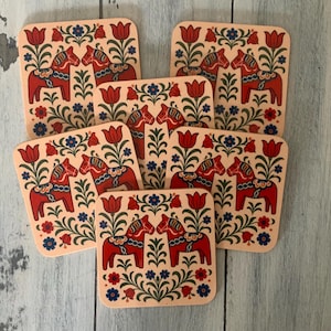 K&ouml;nnte beinhalten: Set aus sechs quadratischen Untersetzern mit traditionellem schwedischen Dala-Pferdemotiv. Jeder Untersetzer zeigt ein rotes Pferd mit blauen und wei&szlig;en floralen Akzenten auf cremefarbenem Hintergrund. Die Untersetzer sind ca. 10 cm gro&szlig;.