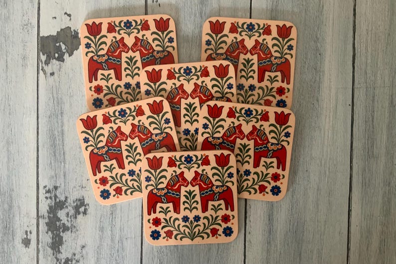 K&ouml;nnte beinhalten: Set aus sechs quadratischen Untersetzern mit traditionellem schwedischen Dala-Pferdemotiv. Jeder Untersetzer zeigt ein rotes Pferd mit blauen und wei&szlig;en floralen Akzenten auf cremefarbenem Hintergrund. Die Untersetzer sind ca. 10 cm gro&szlig;.