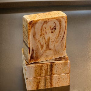 Puede incluir: Tres barras de jabón hechas a mano con un diseño marmoleado marrón y blanco. El jabón está apilado uno encima del otro.