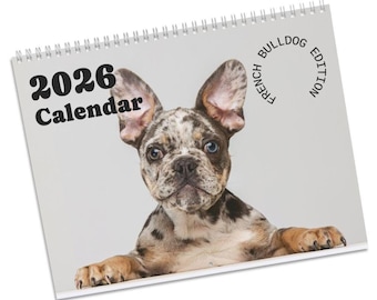 May include: A spiral-bound 2026 calendar featuring a close-up of a French Bulldog puppy. The puppy has a speckled coat of brown, black, and white, with blue eyes. The calendar is labeled "2026 Calendar" and "French Bulldog Edition."