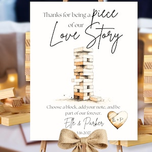 Puede incluir: Un letrero blanco con el texto "Thanks for being a piece of our Love Story" y una ilustración de acuarela de una torre de Jenga. El letrero incluye los nombres "Elle & Parker" y la fecha "5.16.2027". Una cinta de arpillera está en la parte inferior.