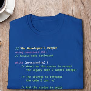May include: A royal blue t-shirt featuring multi-colored programming code text that reads: The Developer's Prayer, using namespace std;, Crisis mode activated, while (programming) { Grant me the syntax to accept the legacy code I cannot change; The courage to refactor the code I can; And the wisdom to avoid