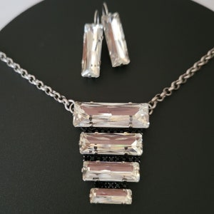 May include: A silver chain necklace with a cascading design of five clear crystal rectangular stones. The necklace comes with a pair of matching earrings with clear crystal rectangular stones.