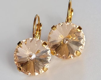 May include: A pair of gold earrings with large, round, light peach-colored crystal stones. The stones have a faceted design and are set in gold.