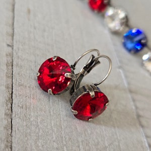 May include: A pair of silver clip-on earrings with red crystal stones. The earrings are a classic style and would be a great addition to any jewelry collection.