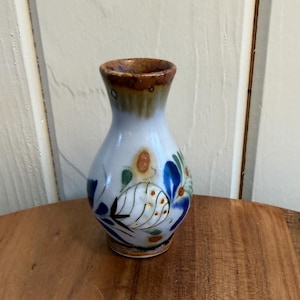 May include: A small, hand-painted ceramic vase with a white base and a brown rim. The vase features blue, green, and orange floral designs. The vase is approximately 4 inches tall.