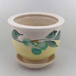 May include: A white ceramic mug with a black handle and the text "But First, Coffee" in a bold, black font. The mug is set against a blurred background, suggesting a cozy setting.