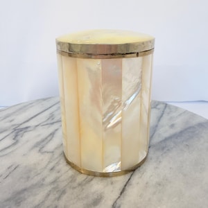 May include: A cylindrical container featuring vertical panels of iridescent mother-of-pearl inlay. The vessel is accented with a polished gold-toned metal rim at the top and base, and it includes a matching circular lid with a smooth, rounded surface.