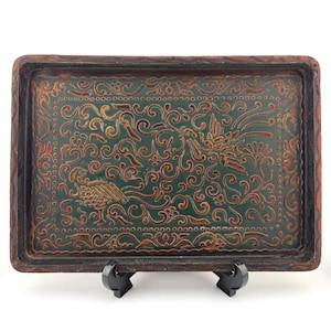 May include: A rectangular tray with a dark green center featuring an intricate, carved relief pattern of two birds surrounded by swirling floral motifs. The tray has a thick, dark brown, textured border with a scalloped edge design.