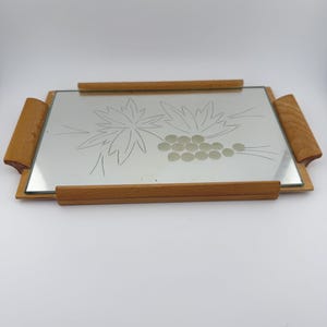 May include: A rectangular serving tray with a mirrored surface and wooden frame. The mirror features an etched design of leaves and grapes. The tray has wooden handles on each end. The tray measures approximately 16 inches long and 10 inches wide.