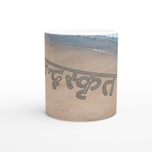 Può includere: Tazza in ceramica bianca con un design a scena di spiaggia. La tazza presenta la parola "Sanskrit" scritta in un carattere simile alla sabbia, sullo sfondo di una spiaggia sabbiosa e onde dell'oceano, creando un'estetica serena.
