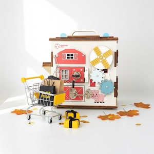 May include: A wooden activity cube with barn and gear designs, featuring a pig illustration. A yellow shopping trolley with Black Friday bags and yellow gift boxes are in front of the cube. Autumn leaves and gold confetti are scattered around.