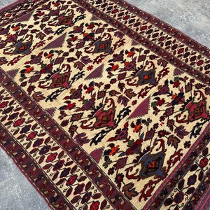 May include: A traditional Persian rug with a cream background and intricate floral patterns in shades of red, burgundy, and blue. The rug has a border of burgundy and cream with a repeating leaf design.
