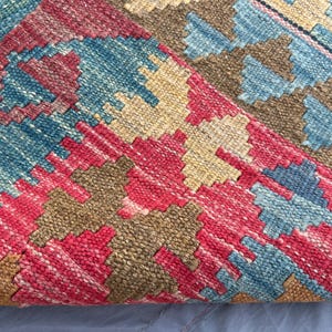 K&ouml;nnte beinhalten: Nahaufnahme eines gewebten Teppichs mit geometrischem Muster. Der Teppich weist eine Kombination aus roten, blauen, beigen und braunen Farben auf. Das Design umfasst Rauten und Zickzackformen, wodurch eine strukturierte Oberfl&auml;che entsteht.