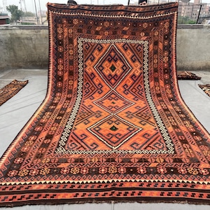 May include: Large, rectangular rug with a geometric pattern in shades of orange, brown, and black. The rug features diamond and zigzag designs, with a border of repeating shapes. Several smaller matching runners are also visible.