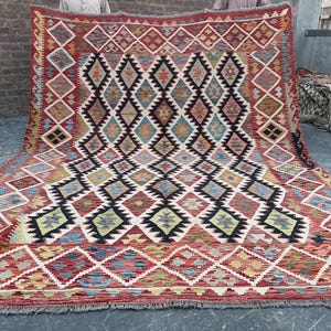 Op de afbeelding: Een traditioneel Turks tapijt met een geometrisch patroon in tinten rood, blauw en beige. Het tapijt heeft een ruitpatroon met ingewikkelde details en een gefranst randje.