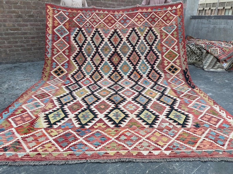 Op de afbeelding: Een traditioneel Turks tapijt met een geometrisch patroon in tinten rood, blauw en beige. Het tapijt heeft een ruitpatroon met ingewikkelde details en een gefranst randje.