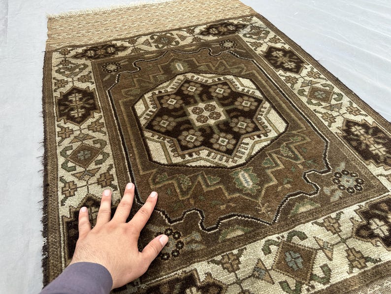 Puede incluir: Una alfombra rectangular marr&oacute;n y beige con un intrincado patr&oacute;n geom&eacute;trico. La alfombra presenta un dise&ntilde;o de medall&oacute;n central con motivos florales y un borde con formas geom&eacute;tricas repetidas. La alfombra tiene un borde con flecos.