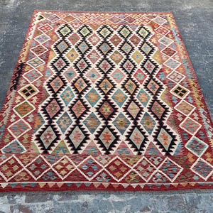 Op de afbeelding: Een traditioneel Turks tapijt met een ruitpatroon in tinten rood, blauw, groen en beige. Het tapijt heeft een franje rand en is geweven met ingewikkelde details.