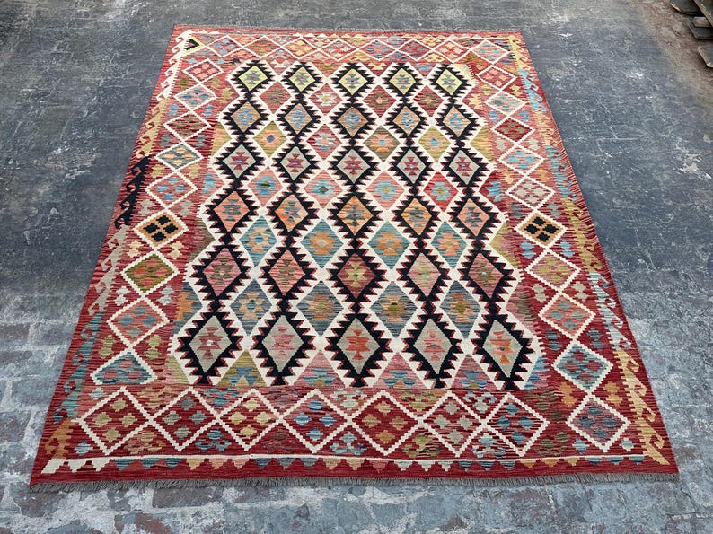 Op de afbeelding: Een traditioneel Turks tapijt met een ruitpatroon in tinten rood, blauw, groen en beige. Het tapijt heeft een franje rand en is geweven met ingewikkelde details.