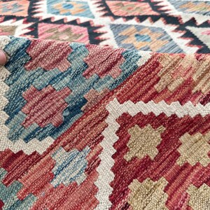 Op de afbeelding: Close-up van een kleurrijk geweven tapijt met een geometrisch patroon in tinten rood, blauw, wit en beige.