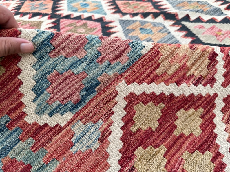 Op de afbeelding: Close-up van een kleurrijk geweven tapijt met een geometrisch patroon in tinten rood, blauw, wit en beige.