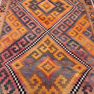 May include: A colorful, geometric patterned rug with a diamond design. The rug features a variety of colors, including orange, yellow, pink, and black. The rug is rectangular and appears to be made of woven material.