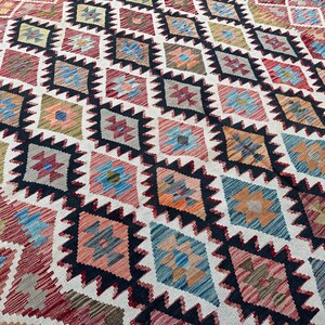Op de afbeelding: Een kleurrijk tapijt met een geometrisch patroon van ruiten en sterren. Het tapijt is geweven met verschillende kleuren, waaronder rood, blauw, groen en geel. Het tapijt is gemaakt van wol en heeft een zachte, pluche textuur.