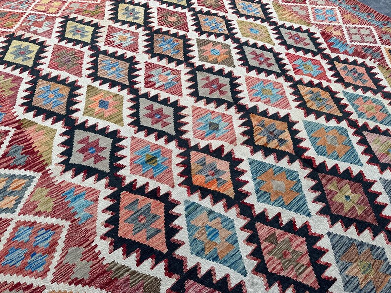Op de afbeelding: Een kleurrijk tapijt met een geometrisch patroon van ruiten en sterren. Het tapijt is geweven met verschillende kleuren, waaronder rood, blauw, groen en geel. Het tapijt is gemaakt van wol en heeft een zachte, pluche textuur.