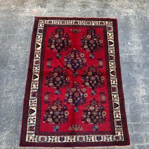 Könnte beinhalten: Ein roter Teppich mit traditionellem persischem Design, das komplizierte Blumenmuster und einen Rand mit geometrischen Motiven aufweist.