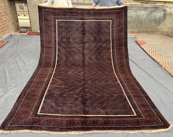 May include: A large, rectangular rug with a dark brown and navy blue geometric pattern. The rug has a cream-colored border and fringe along the edges. The design features diamond and floral motifs.