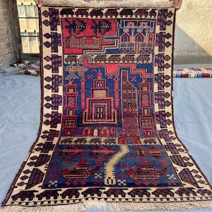 May include: A hand-woven rug with a detailed geometric design. The rug's central field is deep blue, with red and beige patterns. The border is a darker shade, with repeating motifs. The rug has a fringed edge. The rug's dimensions are in centimeters.